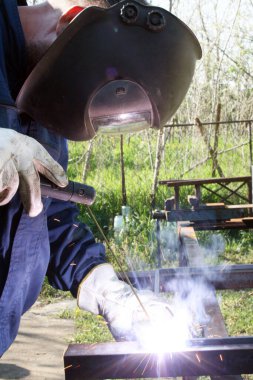Standart koruma ekipmanı takan bir metal parçasını kaynaklıyor.