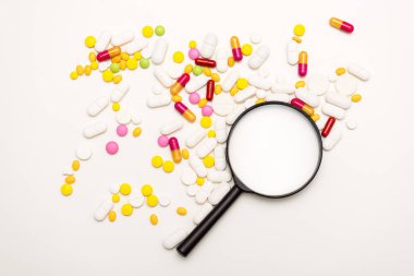 Büyüteç ve beyaz arka planda haplar. Sağlık, tıp ve bilim konsepti. Üst görünüm