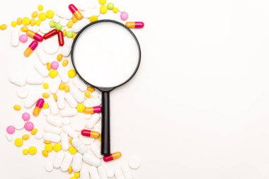Büyüteç ve beyaz arka planda haplar. Sağlık, tıp ve bilim konsepti. Üst görünüm