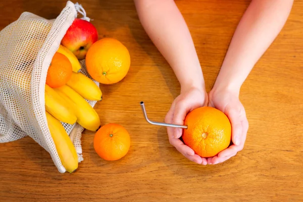 Woman\'s hands holding orange with metal straw in. no plastic concept