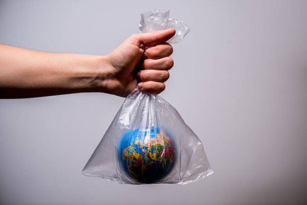 Рука держит пластиковый пакет с глобусом внутри. Эко, экологическая концепция. Ноль отходов
