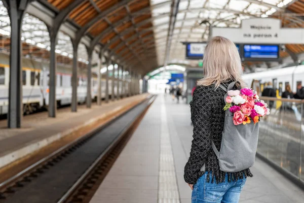 Bir buket çiçekli sırt çantalı genç kadın tren bekliyor. Fotoğraf arkadan..