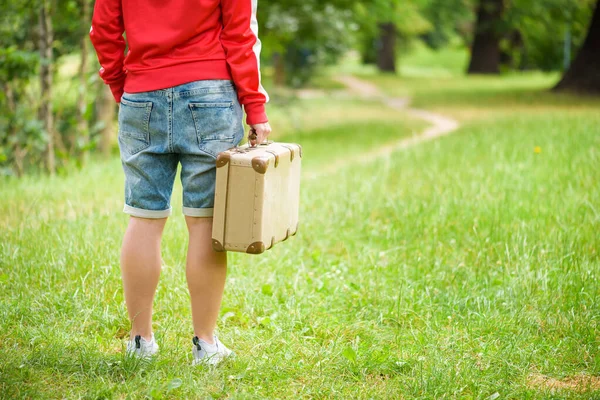 Young person is standing with an vintage suitcase. Photo from the back. Local travel concept