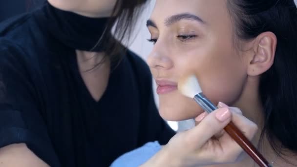Maskérka aplikovat make-up na atraktivní mladé ženy. — Stock video