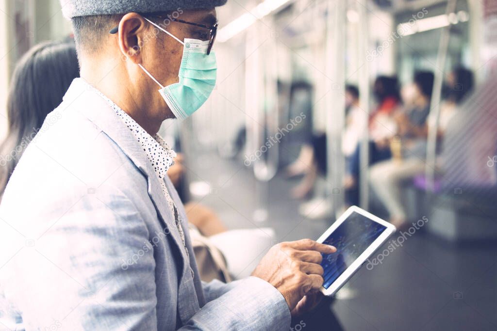 An Asian passenger with a mask to protect CoVid - 19, with a tablet on the train.