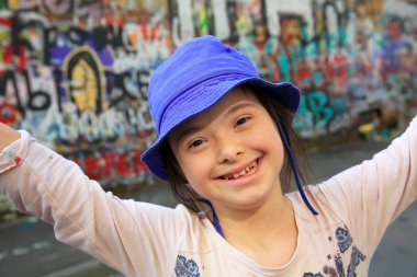 Cute smiling down syndrome girl on the background of the graffiti wall clipart