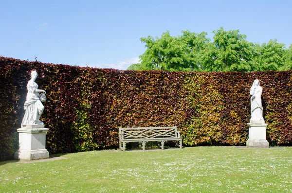 Bank omlijst door standbeelden in formele Engels land tuin — Stockfoto