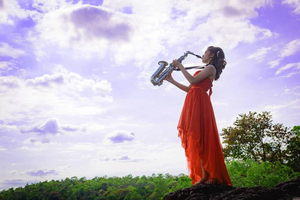 Vacker kvinna bära röd frack ljud saxofon stå på Stockfoto