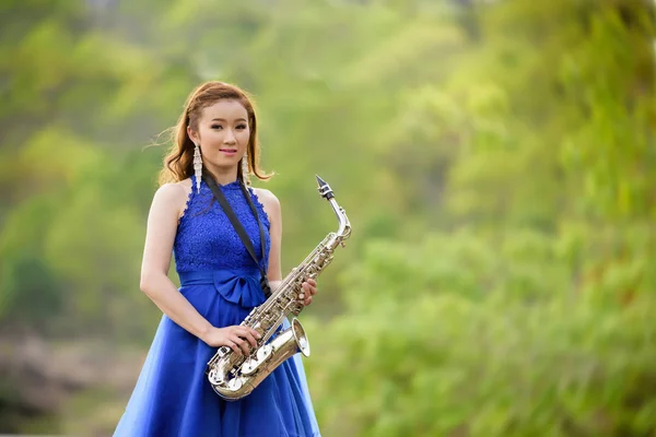 Vacker kvinna slitage blå aftonklänning hålla saxofon stativ Stockbild