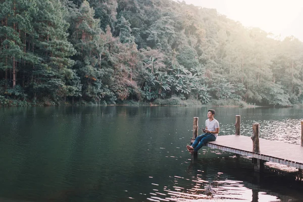 Un hombre se estaba relajando en el puente de madera en la orilla del lago por la tarde —  Fotos de Stock