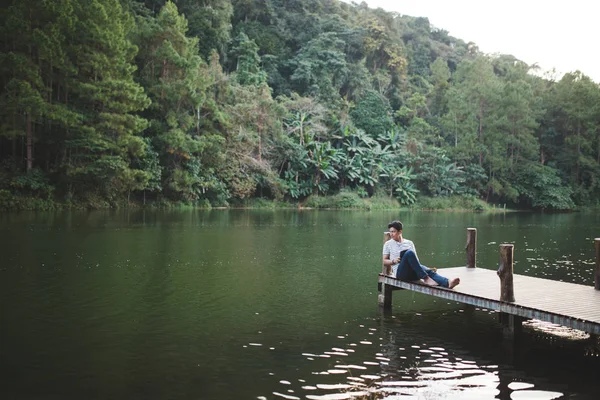 A man sit relaxing on wooden bridge at lakeside in the afternoon — Stock Photo, Image