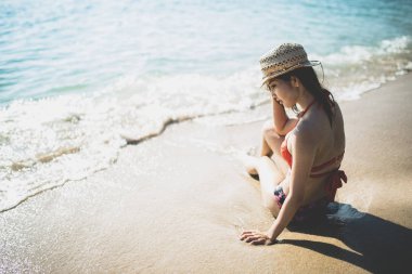 Sahilde oturan kırmızı bikini giyen genç kız.