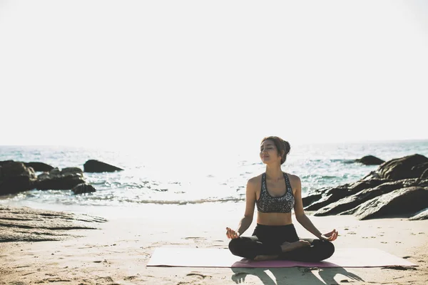 Sahilde yoga yapan genç bir kadın. 
