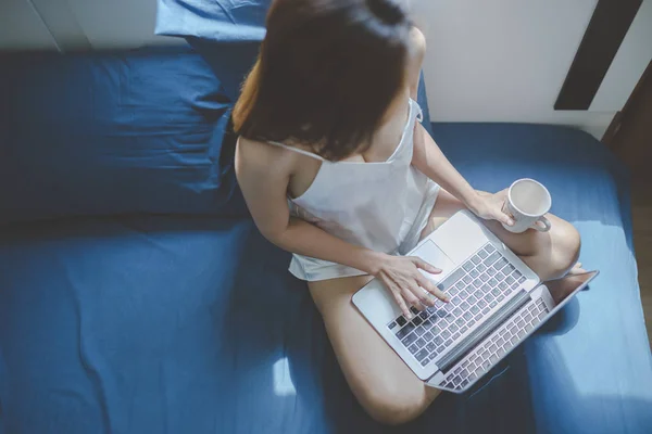 Mujer sosteniendo la taza y el uso de cuaderno en la cama . —  Fotos de Stock