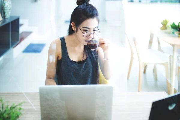 Joven mujer de Asia bebiendo café mientras está sentado trabajando en el ho —  Fotos de Stock