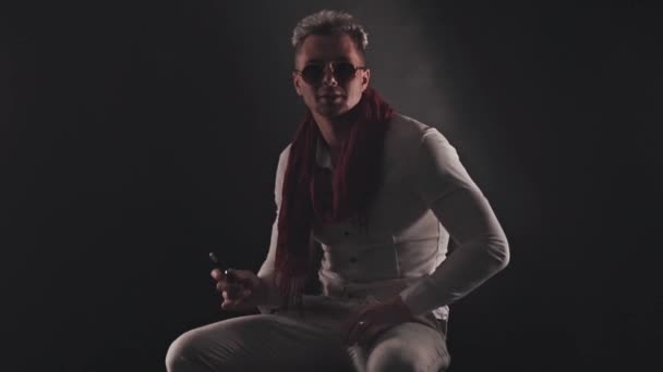 Hombre en una bufanda roja se sienta y fuma un cigarrillo electrónico — Vídeos de Stock