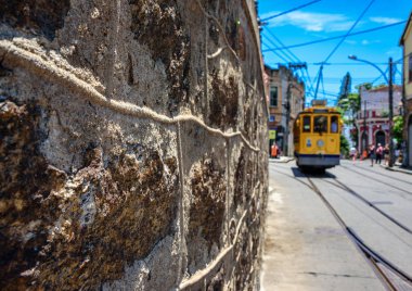 The stone wall, blue sky and old-fashioned yellow tram in Santa Teresa clipart