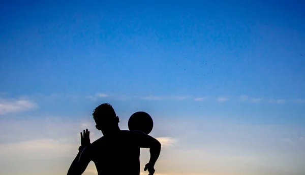 Die Silhouette eines Mannes, der am Strand der Copacabana, Rio de Janeiro, Brasilien, vor blauem Himmel bei Sonnenuntergang den Ball spielt — Stockfoto