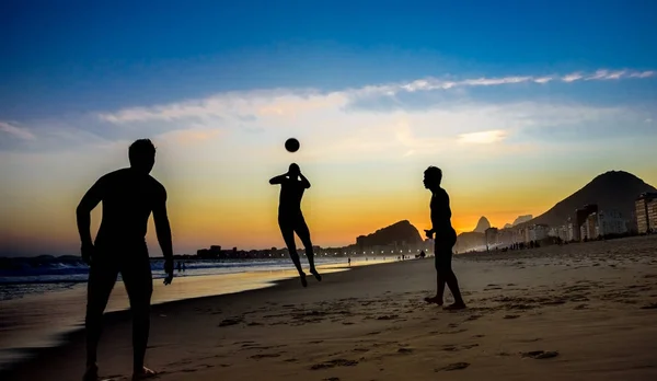 Siluetas de tres hombres jugando fútbol de playa en el fondo de la hermosa puesta de sol en la playa de Copacabana, Río de Janeiro — Foto de Stock