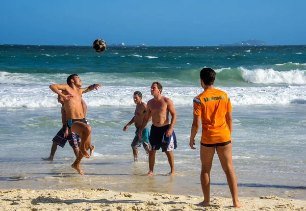 6 diciembre 2016. Tres hombres brasileños jugando fútbol de playa en movimiento en el fondo de las olas en la playa de Copacabana — Foto de Stock