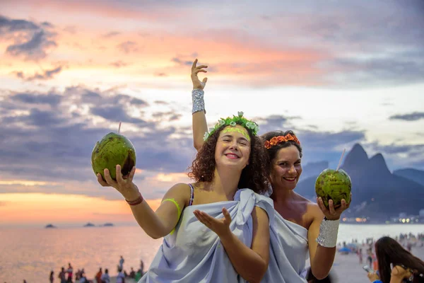 Zwei Frauen in den Kostümen griechischer Göttinnen vor dem Hintergrund des wunderschönen Sonnenuntergangs am Strand von Ipanema, Karneval — Stockfoto
