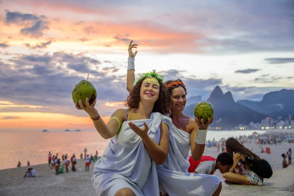 Zwei Frauen in den Kostümen griechischer Göttinnen vor dem Hintergrund des wunderschönen Sonnenuntergangs am Strand von Ipanema, Karneval — Stockfoto