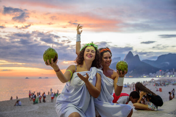 Two women in the costumes of Greek Goddesses on the background of the beautiful sundown at Ipanema beach, Carnaval