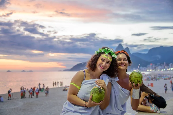 Zwei Frauen in den Kostümen griechischer Göttinnen vor dem Hintergrund des wunderschönen Sonnenuntergangs am Strand von Ipanema, Karneval — Stockfoto