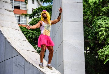 Pembe taç, sarı peruk, tek parça streç giysi ananas ve parlak pembe tutu etek Memorial Getúlio Vargas'ın üzerine duran genç adam