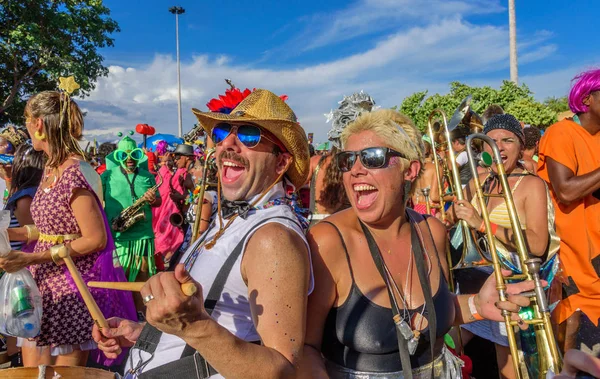 Hombre y mujer divertidos de Bloco Orquestra Voadora tocando tambor y trombón, cantando y bailando en el fondo de otros músicos — Foto de Stock