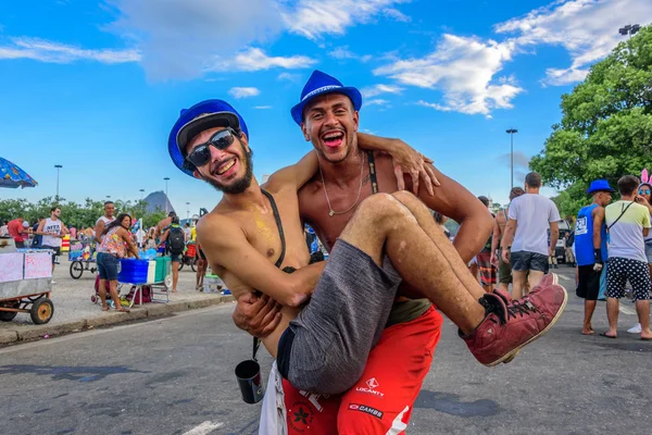 Un hombre sosteniendo a otro hombre en brazos en el fondo de la montaña Sugarloaf durante el Bloco Orquestra Voadora, Carnaval 2017 — Foto de Stock