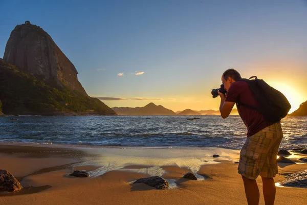 Fotógrafo de viagem ao ar livre no trabalho, tirando fotos da montanha de Pão de Açúcar ao nascer do sol na costa do Oceano Atlântico — Fotografia de Stock