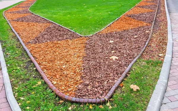 View of colorful orange and brown sawdust in flower bed and green lawn with dry autumn leaves — Stock Photo, Image