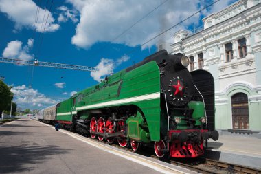 Yeşil buharlı lokomotif, kırmızı tekerlekler platforma geliyor.