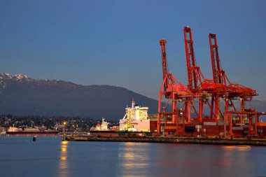 Okyanus gemi yükleme Vancouver, seaport akşam gökyüzü ve bir dağ sırtı arka planı altında. North Vancouver gece ışıkları bir dağ Sırtı'nın eteklerinde.