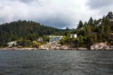 Kıyı şeridi ve bulutlu bir gökyüzü arka planı ormanla kaplı bir kayalık yamaç Köyü.