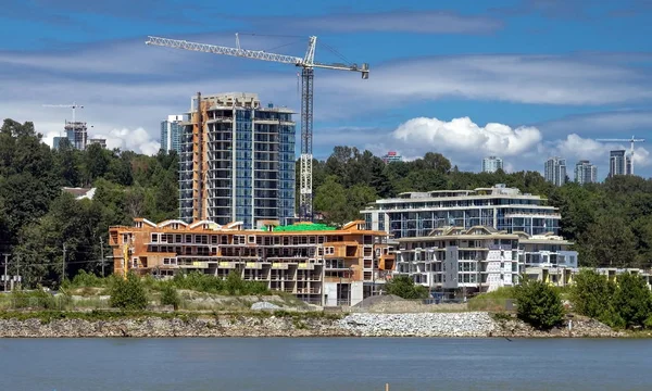 Construction of a new residential district at the riverbank in  Vancouver City. The river bank and the slope covered with forest on the background of a cloudy sky