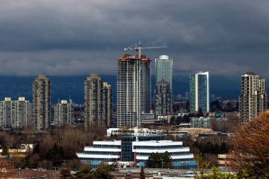 Burnaby şehrinde yüksek binaların yeni inşaatı bir dağ sırtı ve fırtınalı gökyüzünün zeminine karşı.