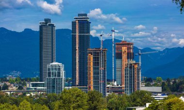 Burnaby şehrinde yeni yerleşim yerinin inşaatı, inşaat ve inşaat halindeki yüksek binalar bir dağ sırtı zeminine karşı vinçler
