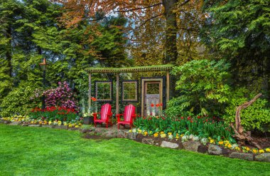 New Westminster City 'deki Queens Park' ta iki kişilik dinlenme yeri. İki koltuk dekoratif oyukta, yeşil çimenlikteki çiçek tarlaları, yayılan ağaçların altındaki çiçek açan çalıların arasında yer alır.