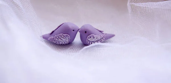 A miniature pair of polymer clay birds in love on white tulle. The concept of love, wedding, union, marriage