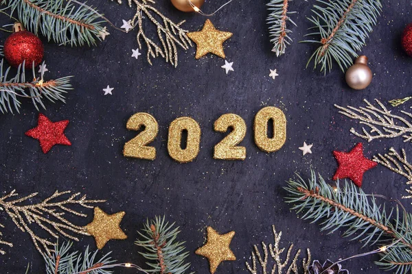 Nytt år platt låg 2020. På en mörk bakgrund, gyllene glänsande siffror 2020 i glitter, grangrenar, julleksaker och en krans. — Stockfoto