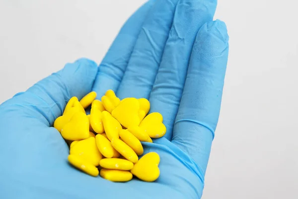 Main dans un gant bleu tient des pilules jaunes en forme de coeur . — Photo