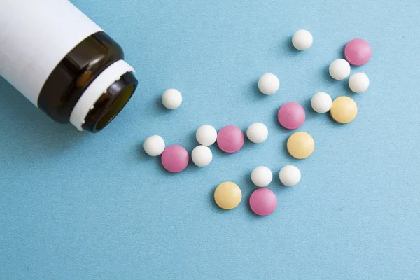 Χάπια διαφόρων χρωμάτων και σχημάτων δίπλα στο μπουκάλι σε μπλε φόντο. Ιατρική έννοια, θεραπεία, υγεία. — Φωτογραφία Αρχείου