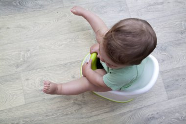 Küçük bir çocuk lazımlığın üzerinde oturuyor. Bebeğe öğretiyorum. 