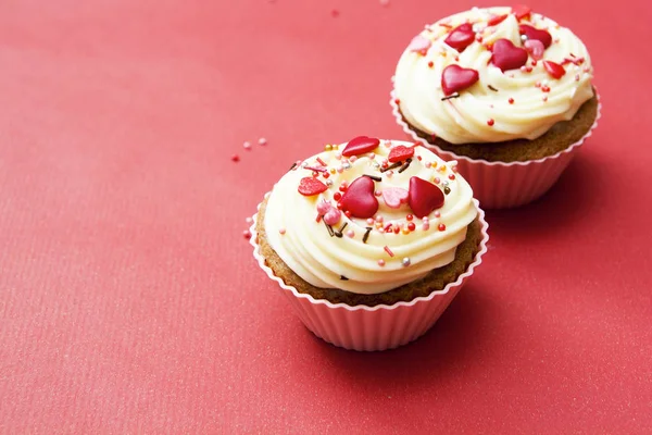 Close-up van twee cupcakes met room en hartdecoratie op een rode bac — Stockfoto