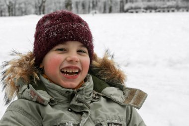 Kış kıyafetleri içinde mutlu bir çocuk ve karlı bir şapka