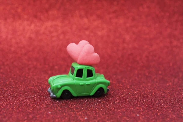 Zabawkowy samochód z dwoma sercami na czerwonym, brokatowym tle. Przestrzeń kopiowania — Zdjęcie stockowe