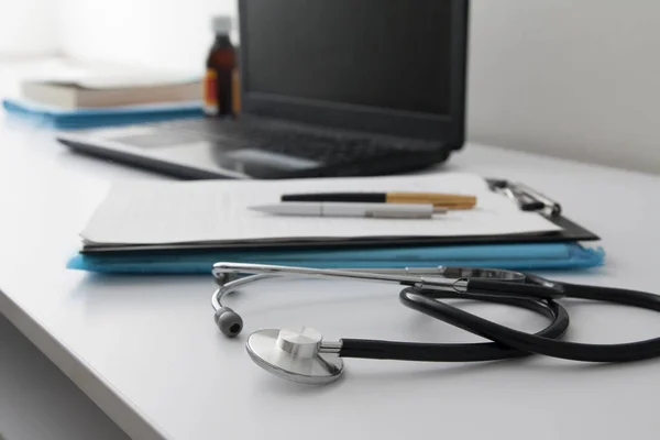 Doctors workplace: close up stethoscope, defocused laptop, documents, pens. Medical concept — 스톡 사진