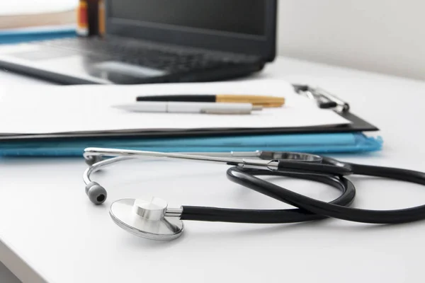 Doctors workplace: close up stethoscope, defocused laptop, documents, pens. Medical concept — 스톡 사진